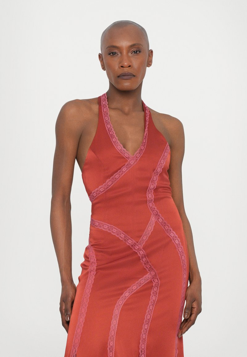 Abito halter in satin rosso con rifiniture in pizzo rosa, design aderente con cuciture diagonali e profondo scollo a V. Texture morbida, silhouette elegante.