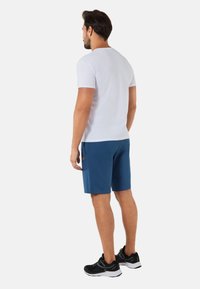 Męska biała koszulka z krótkim rękawem, niebieskie spodenki i czarne buty sportowe. Koszulka ma klasyczny krój; spodenki są do kolan z bocznymi kieszeniami.