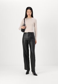 Zwarte faux leren broeken met een hoge taille, gecombineerd met een lichtbeige aansluitend longsleeve top en zwarte stiletto enkellaarsjes.