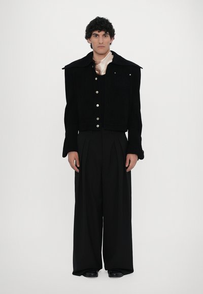 Black corduroy jacket with wide collar, button front, and embroidered detail, paired with high-waisted black trousers. Smooth fabric texture.
