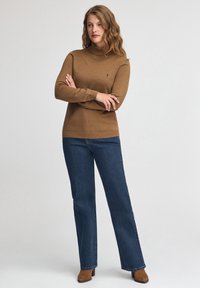 Brauner Strickrollkragenpullover mit gerippten Bündchen und Saum, kombiniert mit dunkelblauen Schlagjeans und braunen Wildleder-Stiefeletten.
