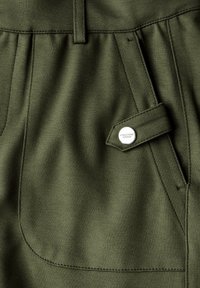 Kapsáčové kalhoty z olivově zelené tkaniny s hladkou texturou, které mají boční kapsu uzavřenou kovovým patentem a výrazné švy.