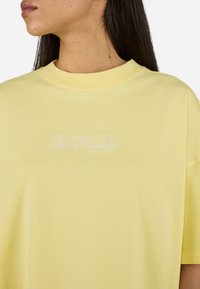 Žluté oversize tričko vyrobené z měkké bavlny, s kulatým výstřihem a vyšitým bílým textem "Regador Club Scent of Summer."