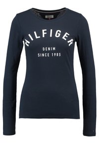 Námořnické tričko s dlouhým rukávem vyrobené z bavlny, se velkým bílým nápisem "HILFIGER DENIM SINCE 1985" na přední straně.