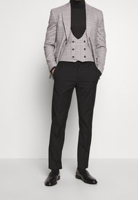 Herrenanzug bestehend aus einem grauen karierten Blazer, einem schwarzen Rollkragenpullover, einer grauen doppeltknöpfigen Weste und einer schwarzen Hose, kombiniert mit eleganten Schuhen.