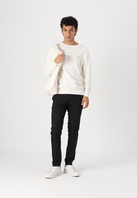 Biały sweter z dzianiny, czarne spodnie slim-fit, białe sneakersy i torba z płótna. Sweter ma małe logo. Prosty i schludny design.