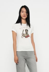 Hvit t-skjorte med korte ermer og et grafisk motiv av hestesko og roser, med «TOMMY JEANS»-tekst i en stilisert font. Mykt bomullsmateriale.
