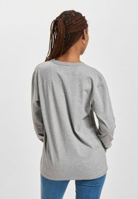 Szary longsleeve z miękkiej bawełny, z okrągłym dekoltem i luźnym krojem, zestawiony z niebieskimi dżinsami.