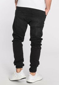 Pantalones vaqueros negros de mezclilla con un ajuste ajustado, con una textura suave y dos bolsillos traseros. Combinados con zapatillas deportivas blancas.