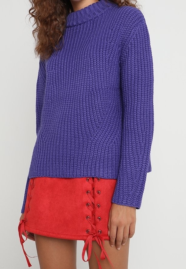 Fialový pletený svetr s vysokým límcem a dlouhými rukávy, doplněný červenou semišovou mini sukni s bočním šněrováním.