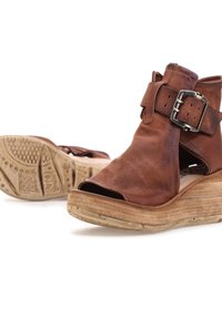 Brune læder wedge-sandaler med åbne tæer, med en bred rem og metalspænde akcent. Tekstureret sål for greb og stabilitet.