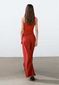 Röd stickad kort topp kombinerad med lösa, vida röda byxor. Outfitten har en texturerad yta och kompletteras av mörka sandaler.