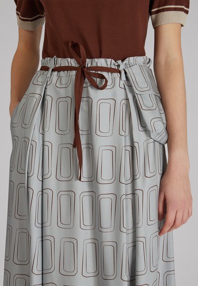 Jupe bleu clair avec un motif rectangulaire brun sur l'ensemble, dotée d'une taille élastique et d'une ceinture en tissu marron nouée.