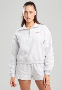 Light gray zip-up sweatshirt with a high collar, featuring red "New York" embroidery and a relaxed fit. Paired with matching shorts.