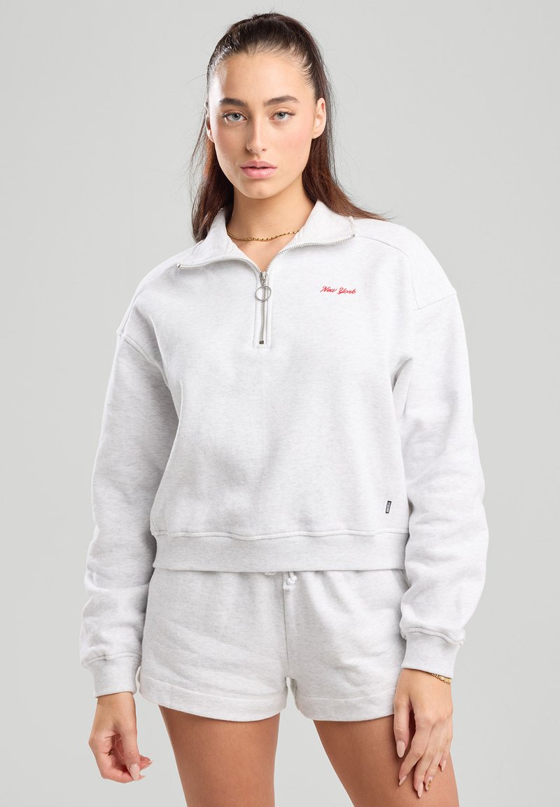 Light gray zip-up sweatshirt with a high collar, featuring red "New York" embroidery and a relaxed fit. Paired with matching shorts.