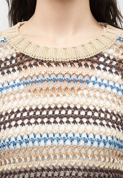 Κοντινό πλάνο ενός υφασμένου πολύχρωμου πλεκτού πάνω μέρους με μπεζ, μπλε και καφέ ρίγες πάνω από ένα λευκό εσώρουχο, που δείχνει τον λαιμό και το πάνω μέρος του στήθους.