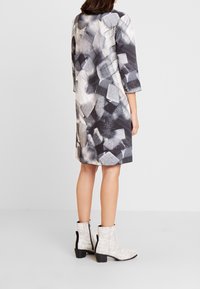 El vestido cuenta con un patrón abstracto monocromático en tonos de gris, con mangas tres cuartos y un corte recto, combinado con botas de tobillo estampadas.