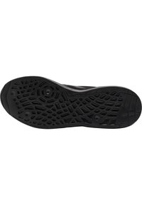 Semelle de chaussure noire en caoutchouc avec des motifs antidérapants texturés, formes circulaires et géométriques, et la marque "hummel" près de la zone de la voûte plantaire.