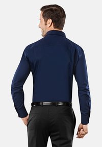 Chemise à manches longues bleu marine avec un col standard, texture lisse, assortie avec un pantalon noir et une ceinture noire. Design minimaliste.