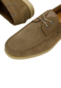 Hellbraune Mokassin-Schuhe aus Wildleder mit beigen Gummisohlen und beigen Schnürsenkeln, die durch Metallösen gefädelt sind.