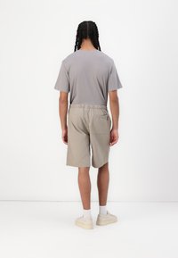 Grå t-shirt med kort ärm och beige shorts med resårmidja, som har en bakficka och avslappnade sneakers, sedd bakifrån.