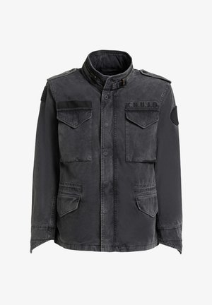 Fekete katonai stílusú dzseki négy elülső zsebfedéllel, magas gallérral és csattal, vállpántokkal, valamint foltdíszítéssel a mellkason és az ujjon.