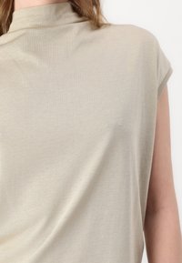 Lys beige topp med høy hals og cap-ermer. Laget av mykt stoff med en glatt tekstur og minimale sømmer.