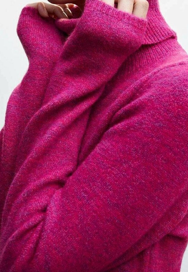 Personne portant un pull rose vif, douillet et texturé, tirant la manche sur une partie de sa main, sur un fond uni.