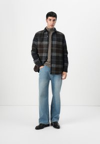 Tumedates checkered flanelljakid beeži ribikrae kõrge kaelusega, koos helesiniste laiade pükstega ja mustade kingadega.