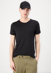 Black short-sleeve t-shirt with a round neckline, paired with tan olive green pants. Background is plain white.