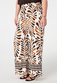Pantalons larges avec un fond crème et un motif de feuilles brunes. Dispose d'une bande noire décorative à l'ourlet. Fabriqués en tissu léger.