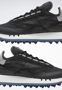 Chaussures de sport noires avec empeignes texturées, semelles intermédiaires blanches, semelles extérieures bleues avec crampons et détails réfléchissants gris au talon, vues de côté.