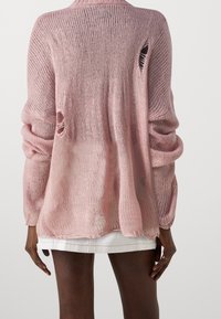 Pull en tricot rose clair avec coupe ample, poignets côtelés et trous visibles à l'arrière. Texture douce et design en maille ouverte.