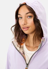 Jasnofioletowa kurtka z kapturem, z zamkiem z przodu i kolorową, wzorzystą podszewką. Gładka tekstura, casualowy design i pewne zamknięcie na suwak.