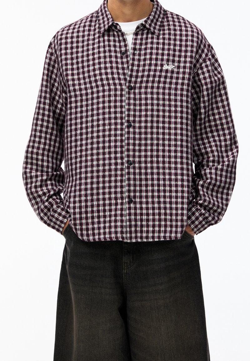 Camicia button-up in fantasia a quadri rossi scuri e bianchi, realizzata in un tessuto dalla texture morbida. Presenta un collo classico e maniche lunghe.
