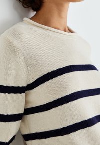 Kremowy sweter dziewiarski w granatowe poziome paski. Posiada okrągły dekolt i luźny krój, ukazując teksturowany materiał.