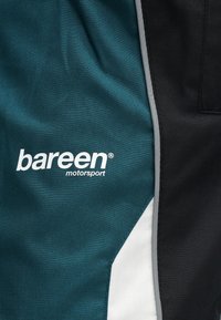 Εγγύς άποψη υφάσματος σε τιρκουάζ, μαύρο και λευκό χρώμα, με λευκό λογότυπο "bareen motorsport" και γκρι επένδυση στη ραφή.