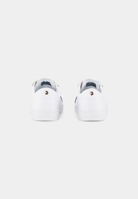 Paire de baskets blanches basses avec le logo de la marque sur le talon et « Hilfiger » embossé sur la semelle, vues de dos sur un fond uni.