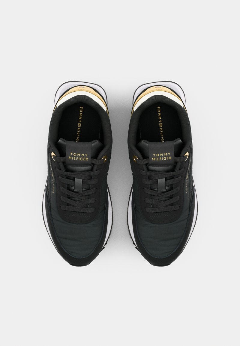 Czarne sneakersy z tekstylną cholewką, złotymi akcentami, sznurówkami i logo na języku. Amortyzowane podeszwy z białą krawędzią i teksturowymi powierzchniami.