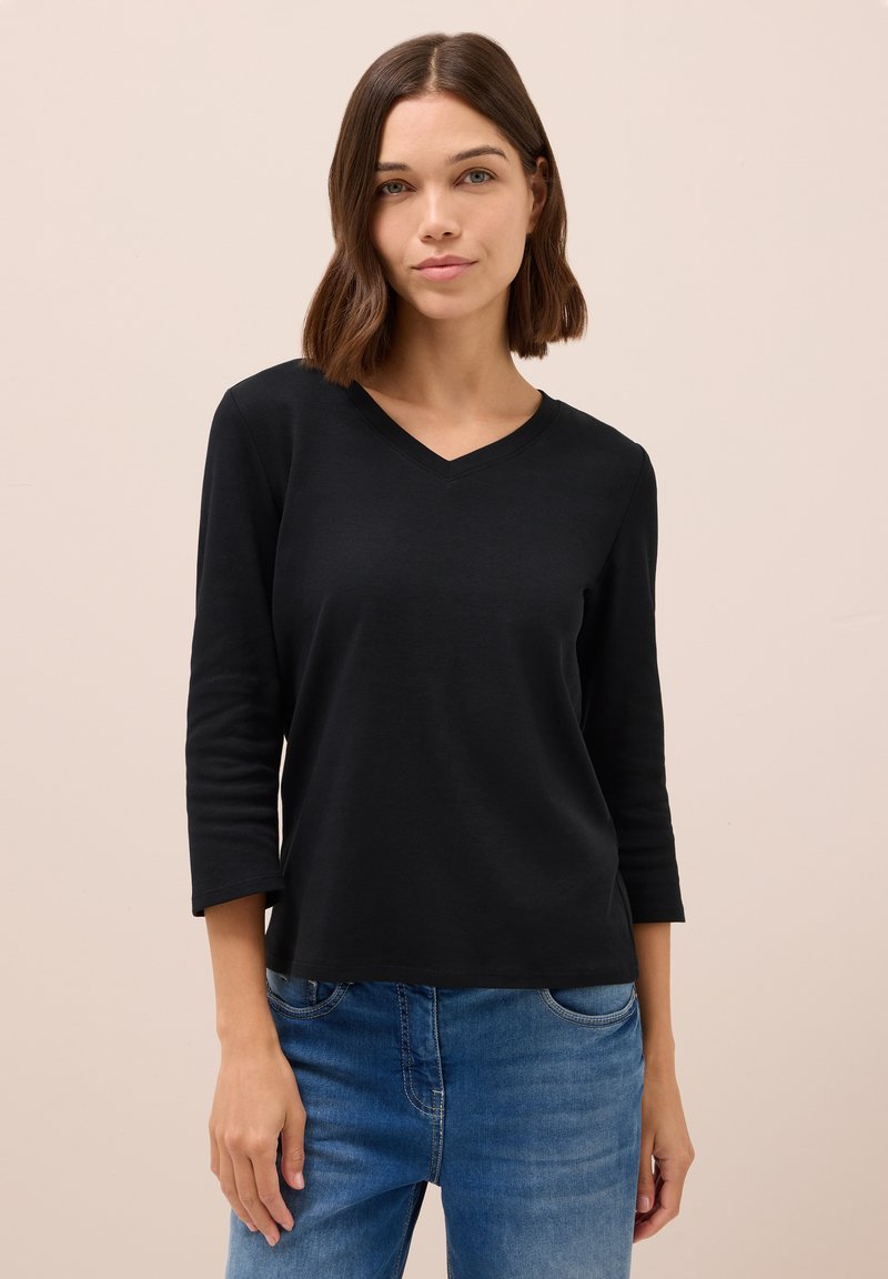 Haut noir à manches longues avec un décolleté en V et une coupe décontractée, fabriqué dans un tissu doux. Associé à un jean en denim bleu.