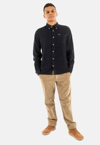 Donkerblauwe corduroy overhemd met een button-down kraag, een voorzak en witte knopen, gecombineerd met tan corduroy broeken en bruine schoenen.