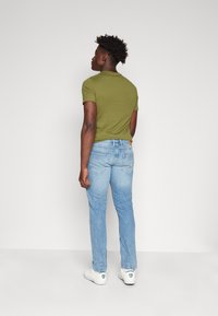T-shirt aderente verde oliva abbinata a jeans azzurri. I jeans presentano una vestibilità classica e tasche posteriori. Sneakers bianche completano il look.
