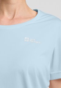 T-shirt azzurro chiaro a maniche corte, realizzato in tessuto liscio. Presenta un logo bianco con il testo "Jack Wolfskin" sulla parte sinistra del petto.