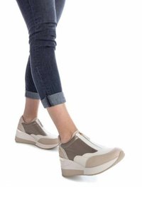 Zapatillas acolchadas en blanco y beige con un acabado texturizado, cierre de cremallera y suela de cuña distintiva, combinadas con jeans de denim enrollados.