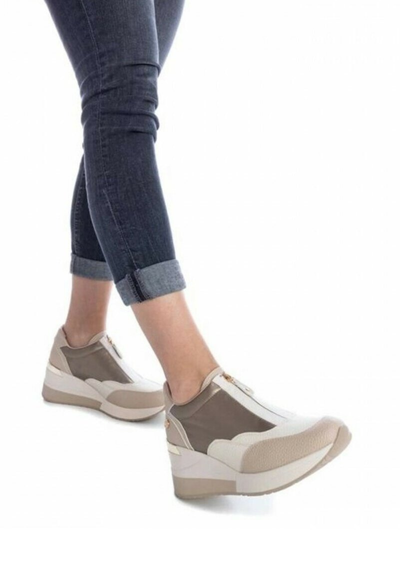 Zapatillas acolchadas en blanco y beige con un acabado texturizado, cierre de cremallera y suela de cuña distintiva, combinadas con jeans de denim enrollados.