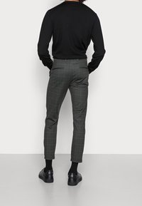 Slim-fit ciemnoszare spodnie z delikatnym wzorem w kratę, z tylnymi kieszeniami, noszone z czarnymi butami i czarną bluzką z długim rękawem.