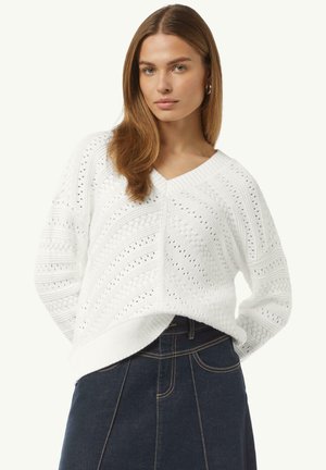 Witte gebreide trui met een V-hals, voorzien van een textuurpatroon en opengewerkte details. Gepaard met een donkerdenimrok.