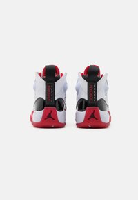 Baskets blanches et noires avec des accents rouges, présentant un talon brillant et une languette noire. Comprend le logo Air Jordan sur le talon.