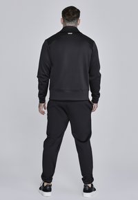 Czarny dres sportowy z zamkiem błyskawicznym, z wysokim kołnierzem, ściągaczami przy mankietach oraz dopasowanymi spodniami z elastycznym pasem.