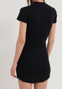 Schwarzes, geripptes Kleid mit kurzen Ärmeln und einer taillierten Silhouette. Es hat einen runden Kragen und einen leicht geschwungenen Saum. Glatte Textur.